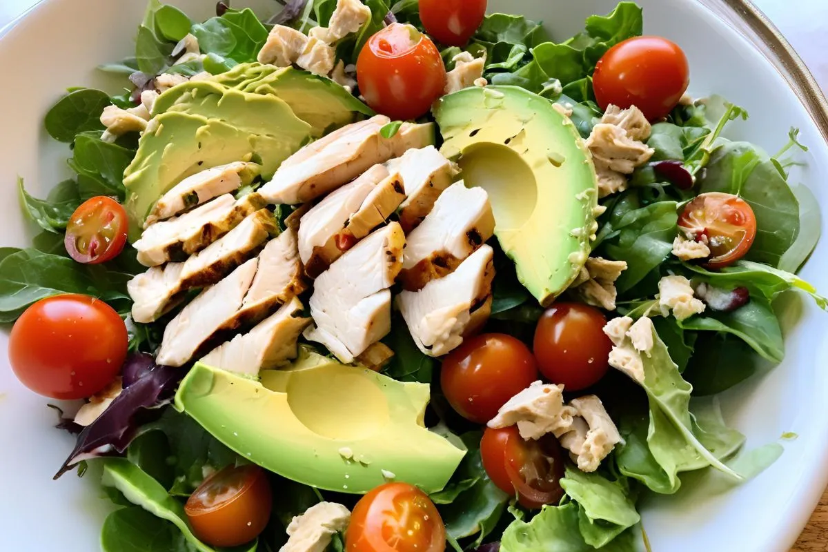 Close-up of a healthy salad recipe with chicken, avocado, and tomatoes.